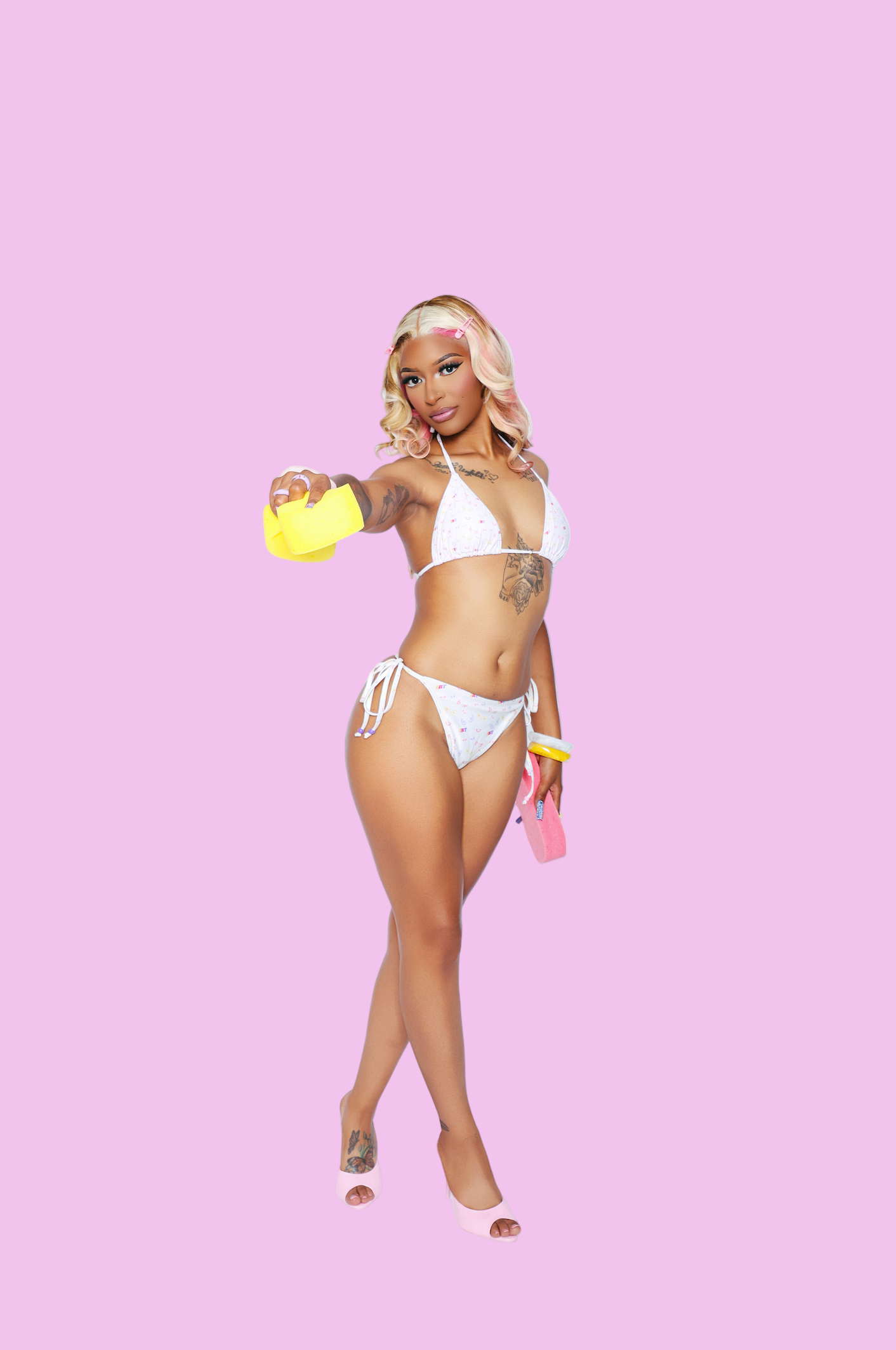 Woman in a white bikini holding a yellow sponge and pink shoes on a white background